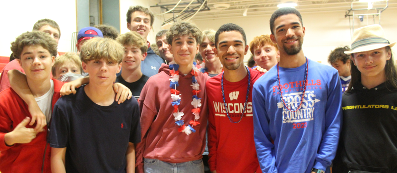 A diverse group of young adults and teenagers pose together indoors, smiling for a group photo.
