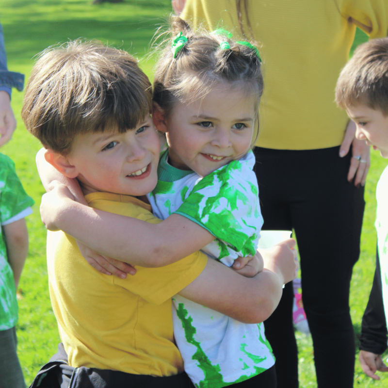 Two young children share a warm hug outdoors on a sunny day.
