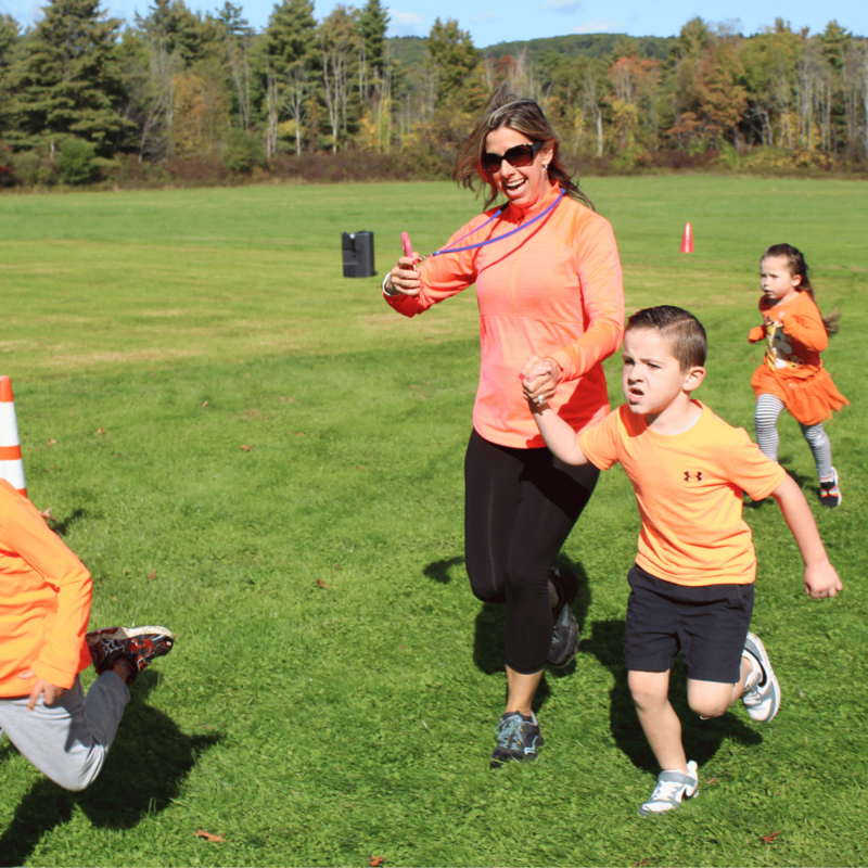 A woman and children run across a sunny, green field wearing matching orange shirts.