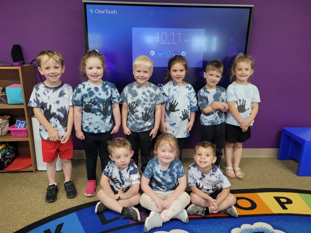 Preschool children from Miss Emily’s class proudly showing their field trip shirts while standing together, smiling and posing for a group photo during an end-of-year activity.