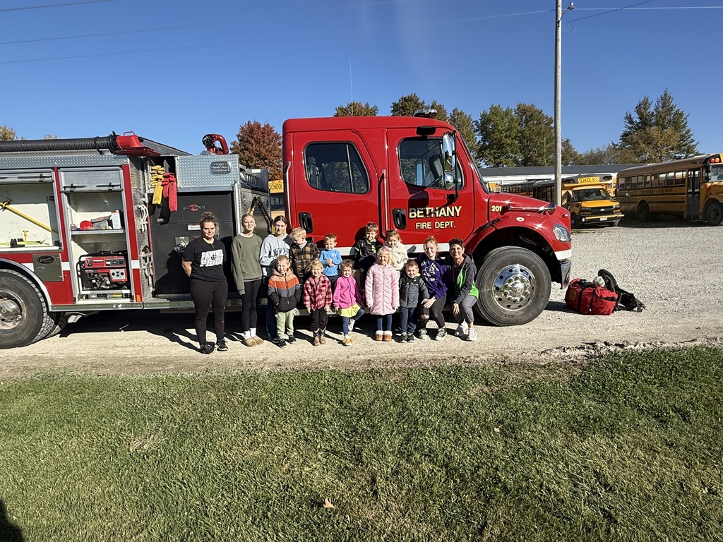 Preschool students learning about fire safety while exploring a fire truck, looking at firefighter equipment, and visiting with firefighters