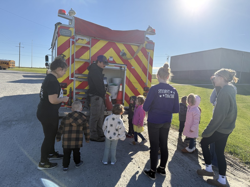 Preschool students learning about fire safety while exploring a fire truck, looking at firefighter equipment, and visiting with firefighters