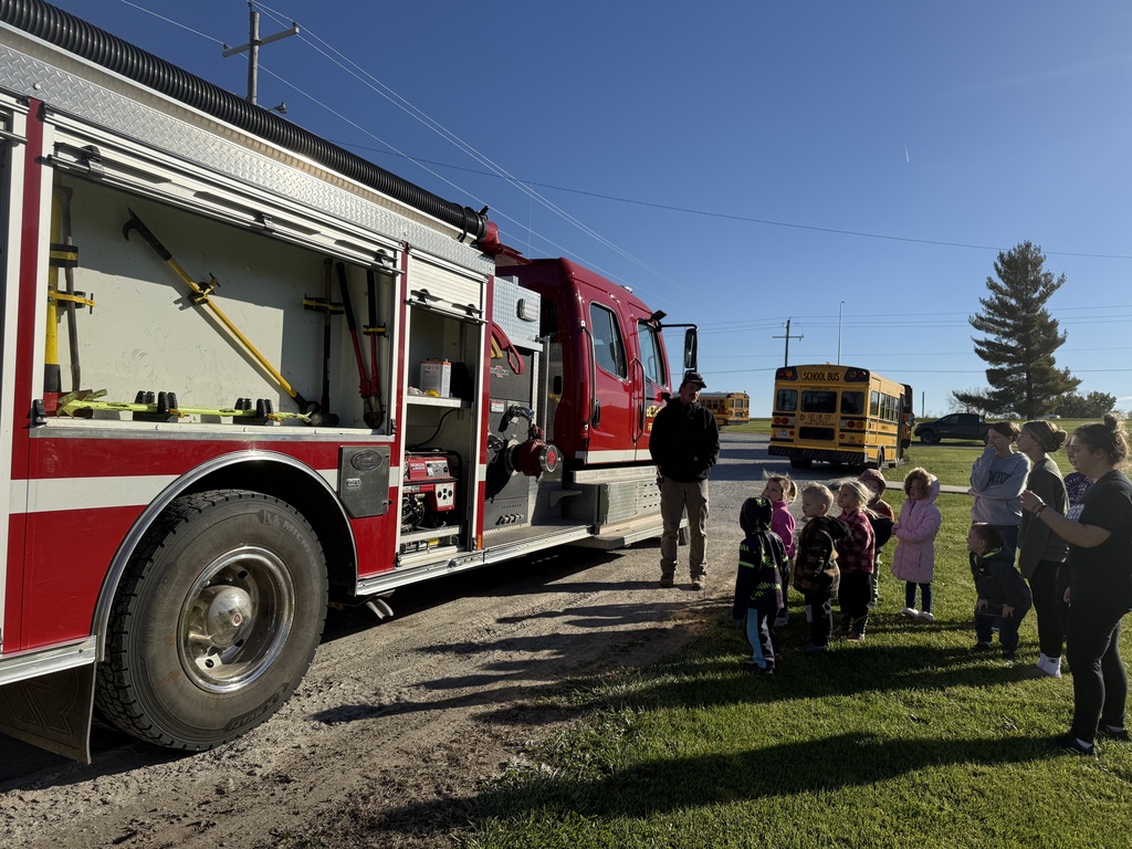 Preschool students learning about fire safety while exploring a fire truck, looking at firefighter equipment, and visiting with firefighters