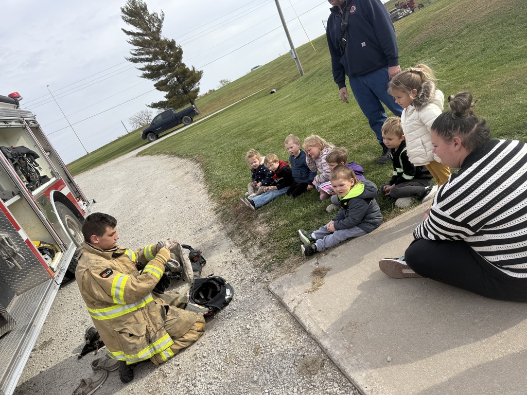 Preschool students learning about fire safety while exploring a fire truck, looking at firefighter equipment, and visiting with firefighters