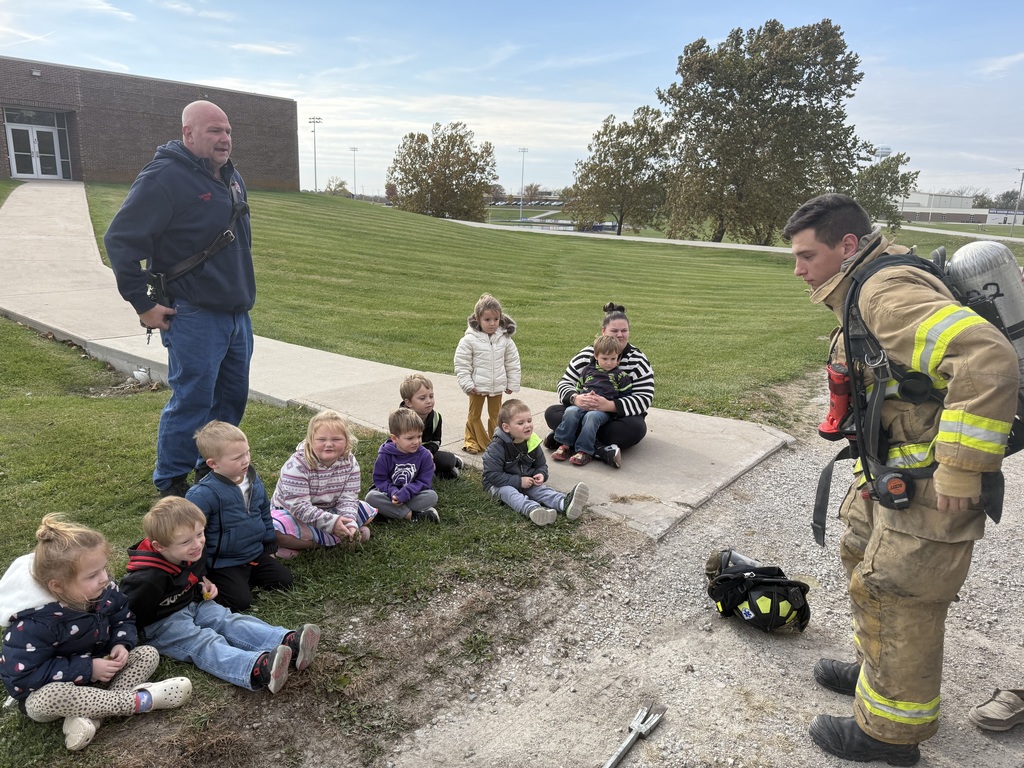 Preschool students learning about fire safety while exploring a fire truck, looking at firefighter equipment, and visiting with firefighters