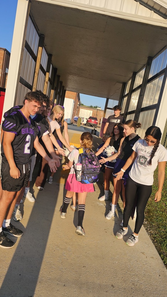 An elementary student walks through the car drop off while giving high fives to high school athletes