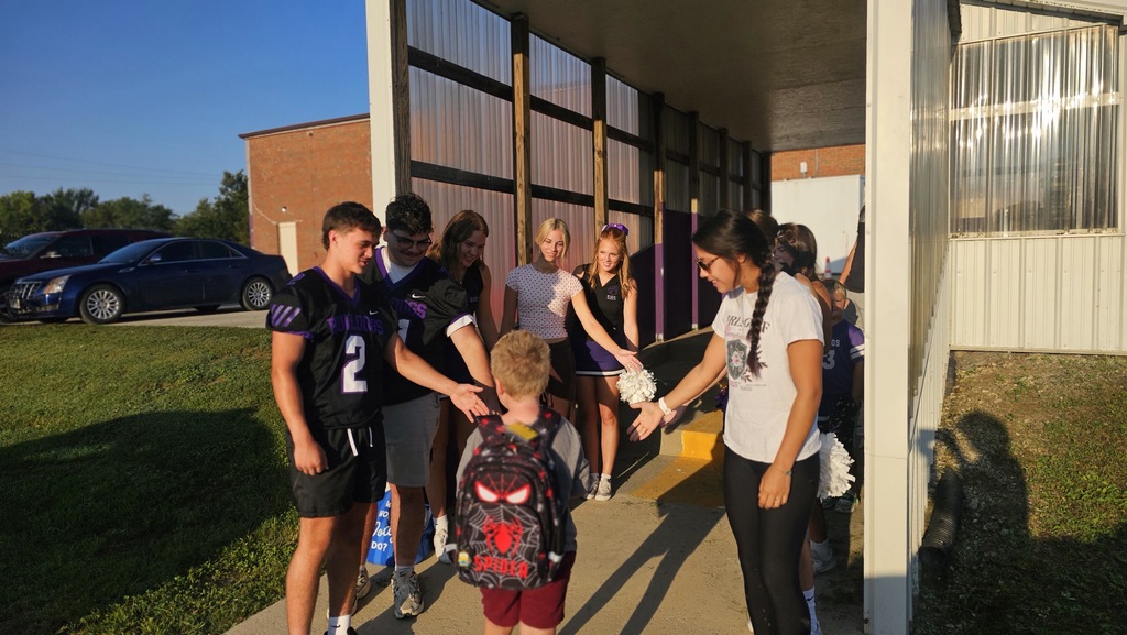 An elementary student walks through the car drop off while giving high fives to high school athletes