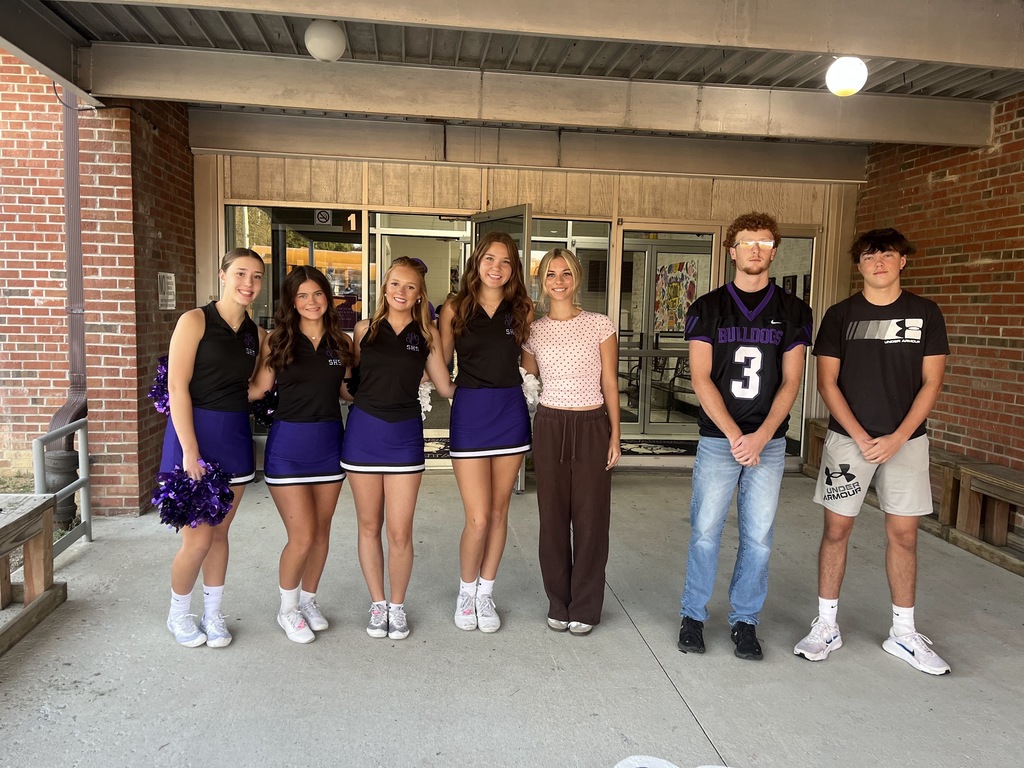 High School Athletes pose together at the front doors of the elementary school