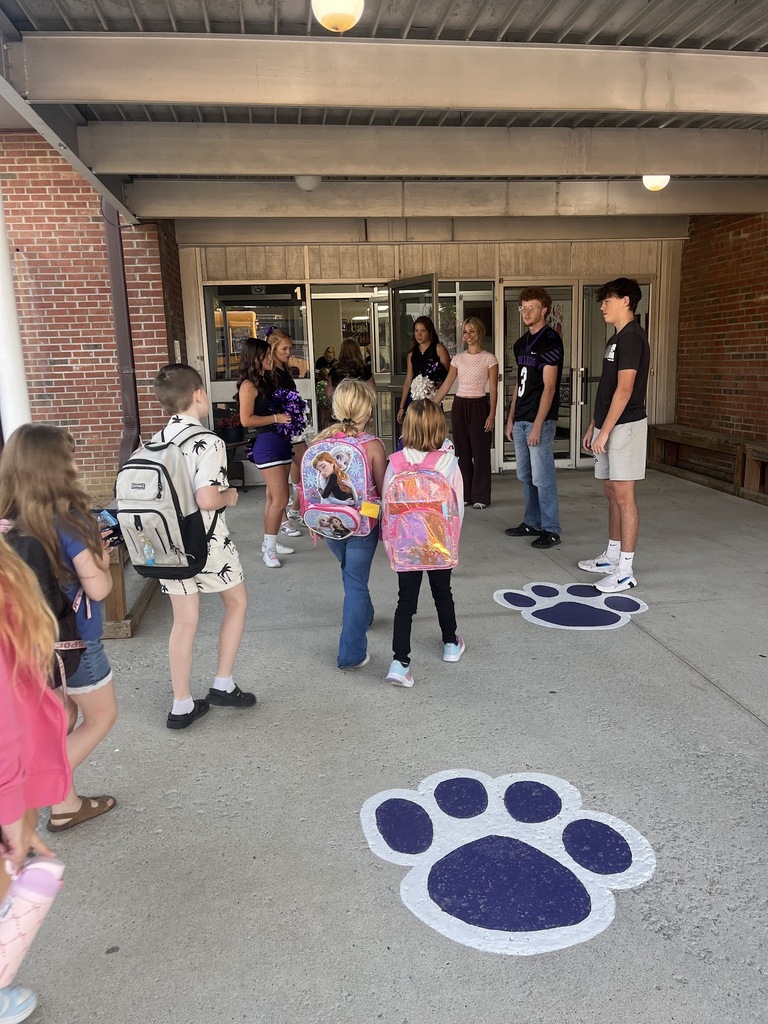 Elementary Students walk through the front doors of the elementary school while High school Athletes greet them.