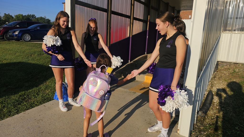 An elementary student walks through the car drop off while giving high fives to high school cheerleaders