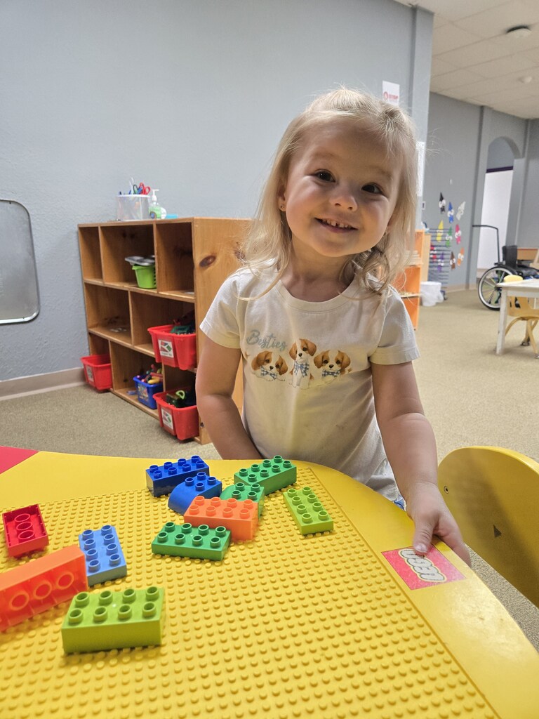 Girl playing with Legos with a big smile.