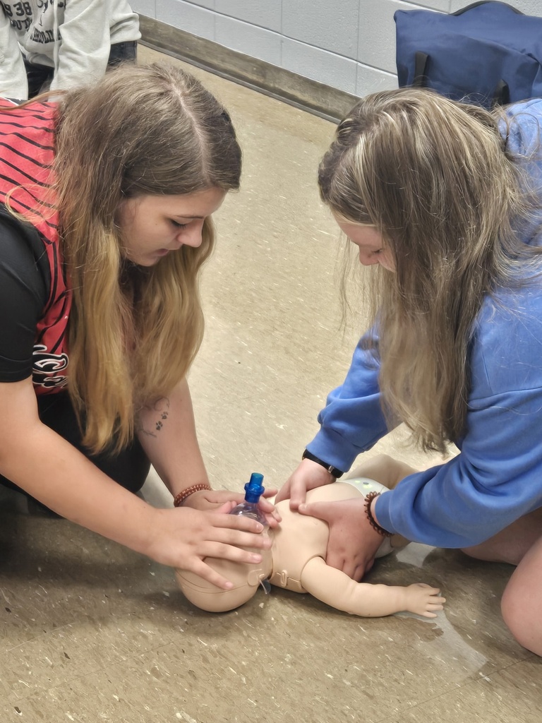 2 students giving breaths to infant.