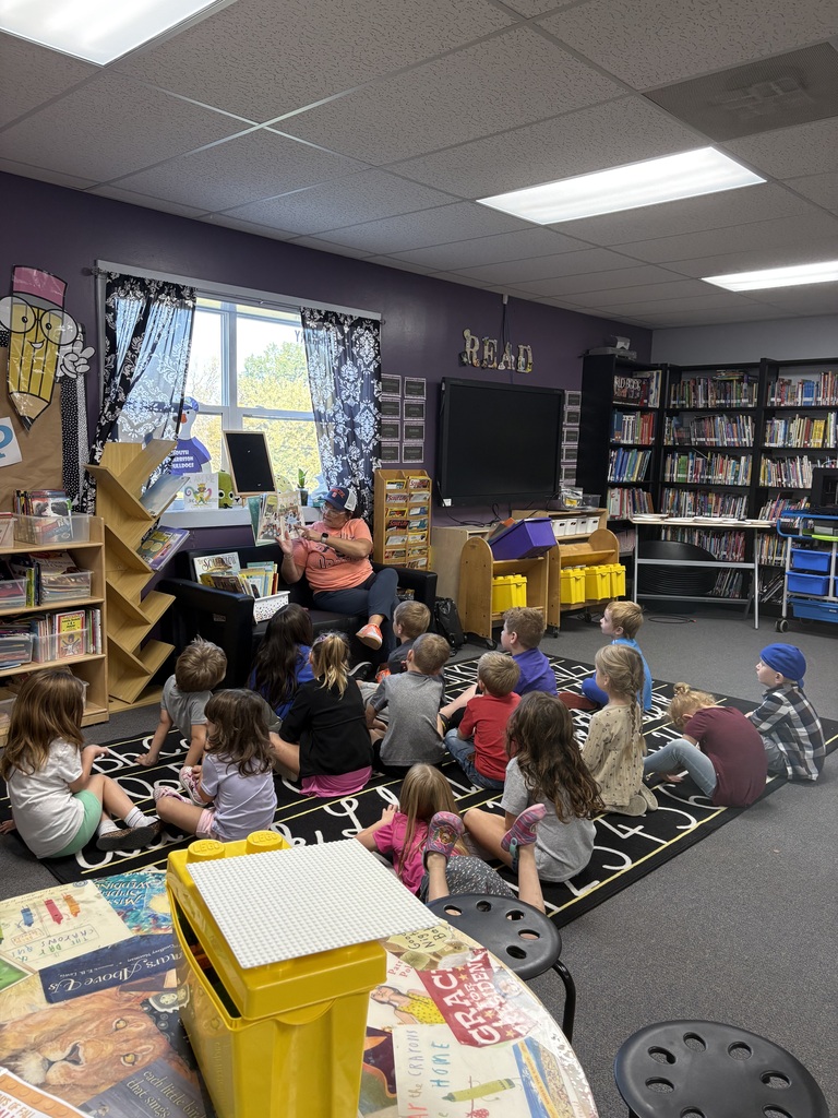 students looking at librarian while she reads a book to them