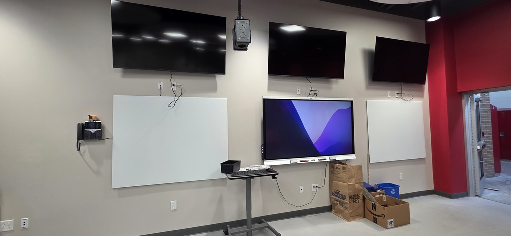 TVs hanging on wall over a smart board and two white boards