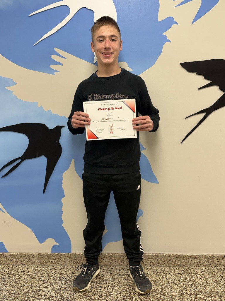 Dawson holds up a student of the month sign while wearing a black sweatshirt, sweatpants and sneakers
