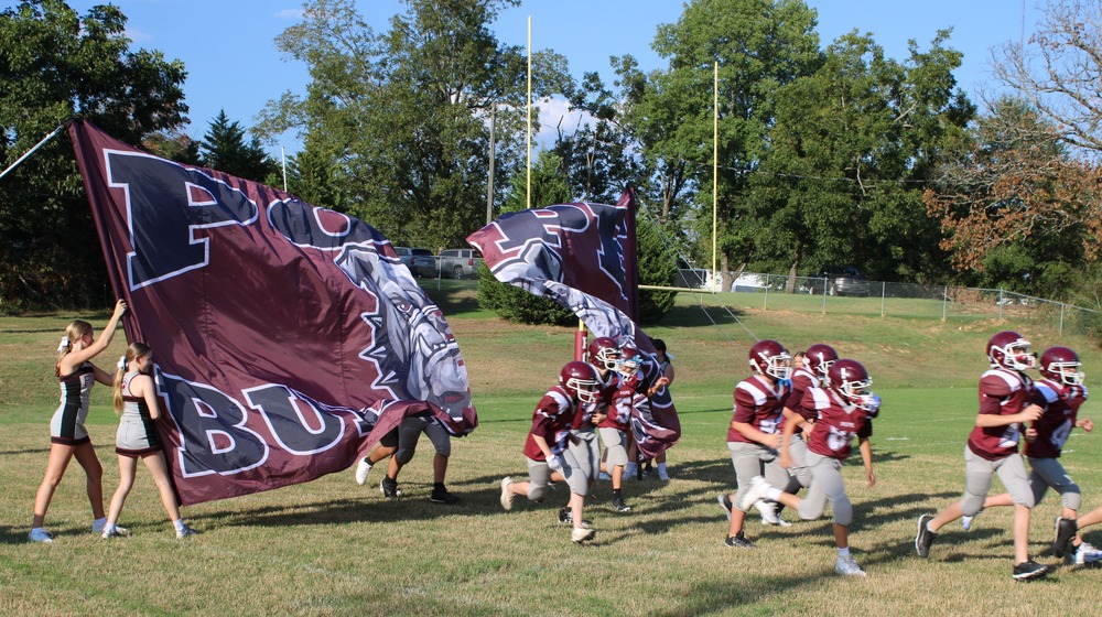 Football team on field running through banner