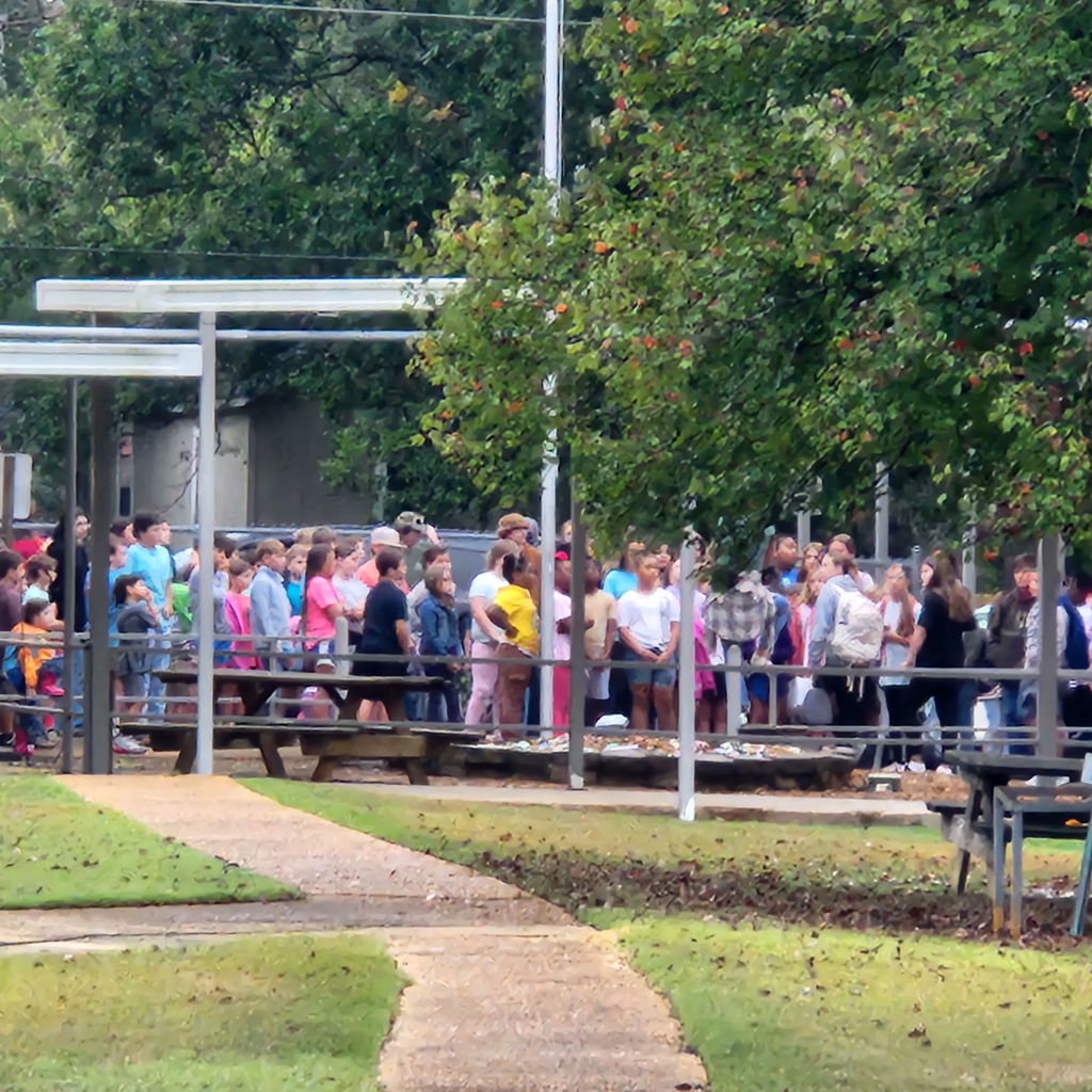 Elementary and junior high students gather outside of a school building