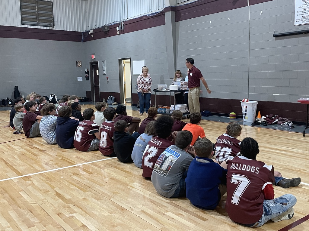 football boys sitting on gym floor listening to speaker