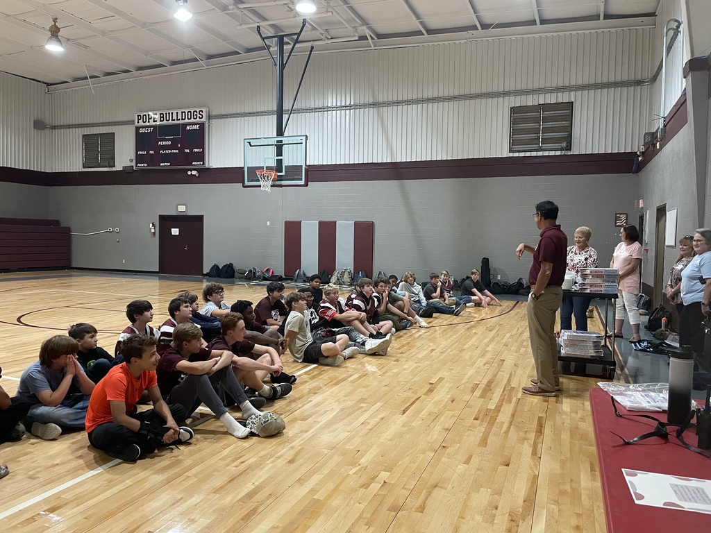 football boys sitting on gym floor listening to speaker