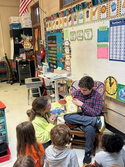 Juior high student reading to a group of 1st graders