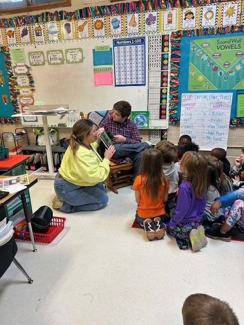Juior high student reading to a group of 1st graders
