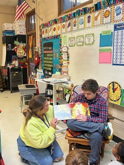 Juior high student reading to a group of 1st graders