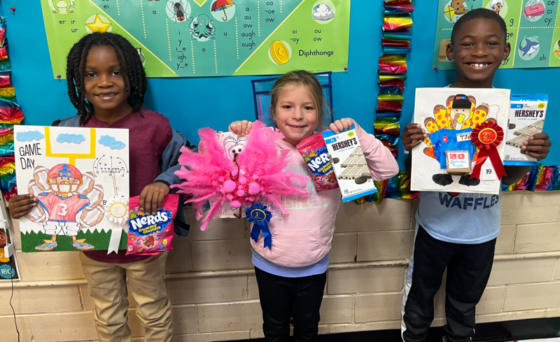 3 elementary students holding art projects
