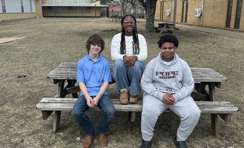 3 students standing in front of a curtain