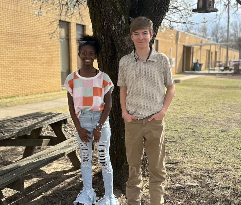 2 students standing in front of a curtain