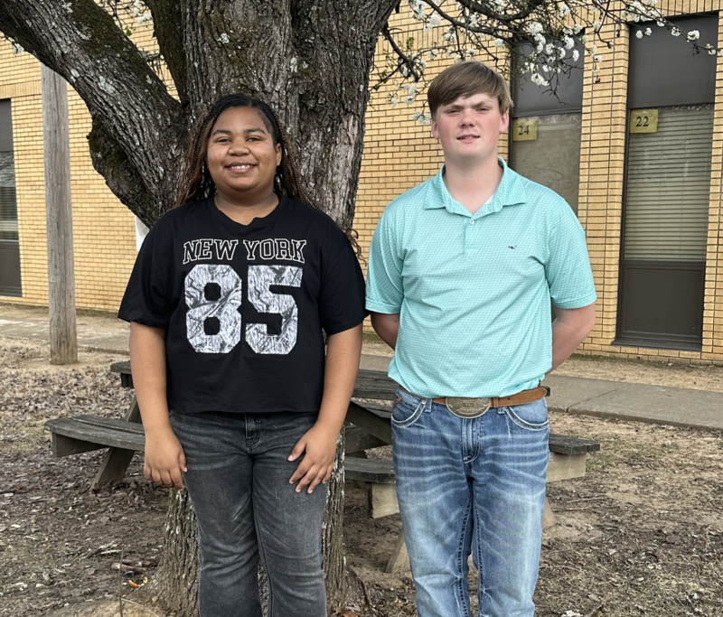 2 students standing in front of a curtain