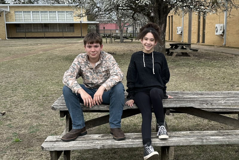 2 students standing in front of a curtain
