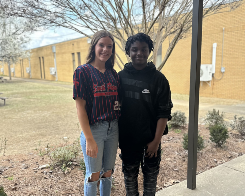 2 students standing in front of a curtain