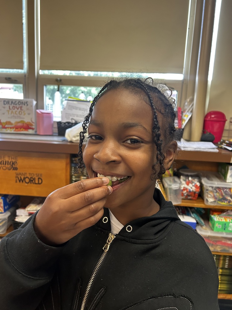 A student smiles while holding a piece of fruit up to their mouth, appearing excited to take a bite