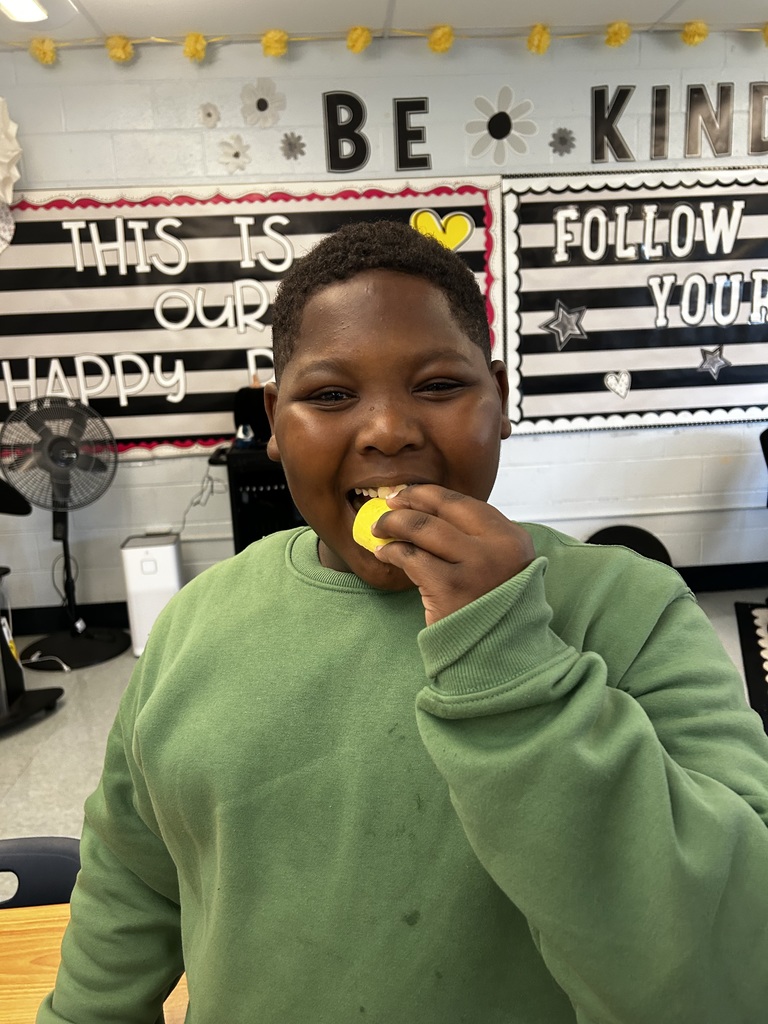 A student in a green sweatshirt smiles widely while taking a bite of a yellow fruit