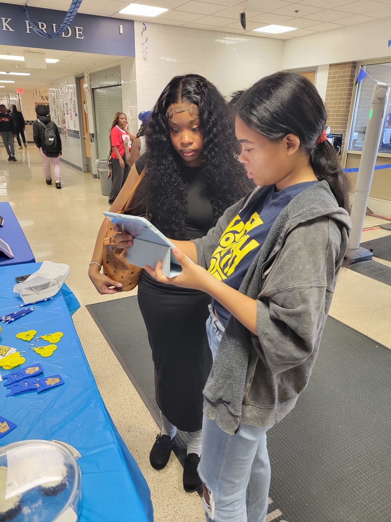 Two students look at a tablet together at a table covered in blue cloth with “PA Youth Vote” materials spread out.