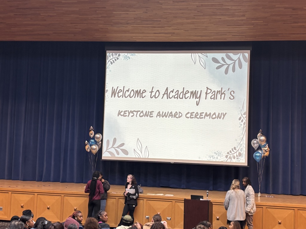A large projection screen on a stage displays the message “Welcome to Academy Park’s Keystone Award Ceremony” with decorative leaf graphics.