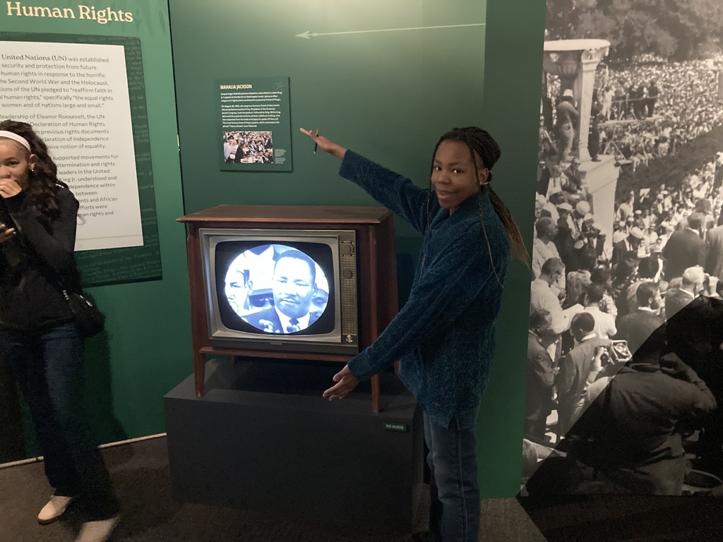 A student poses next to a vintage television displaying a black-and-white image of Martin Luther King Jr., part of a museum exhibit on human rights.