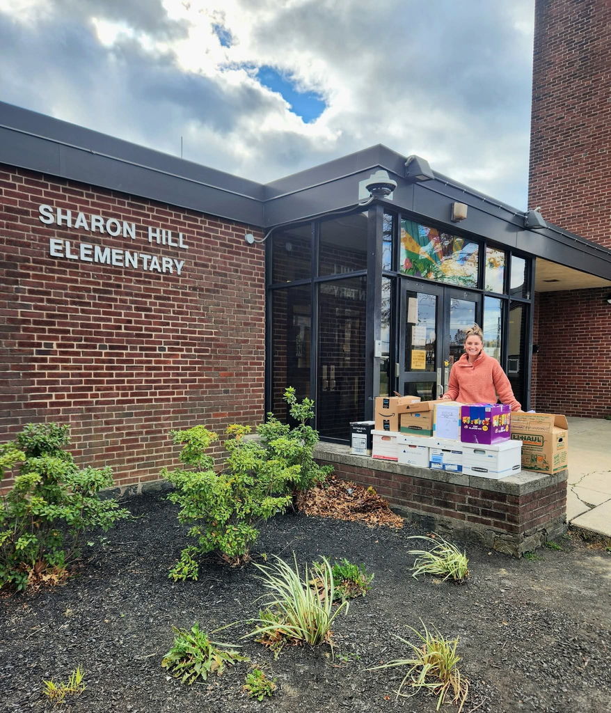 Teacher standing with boxes of books in front of Sharon Hill Elementary