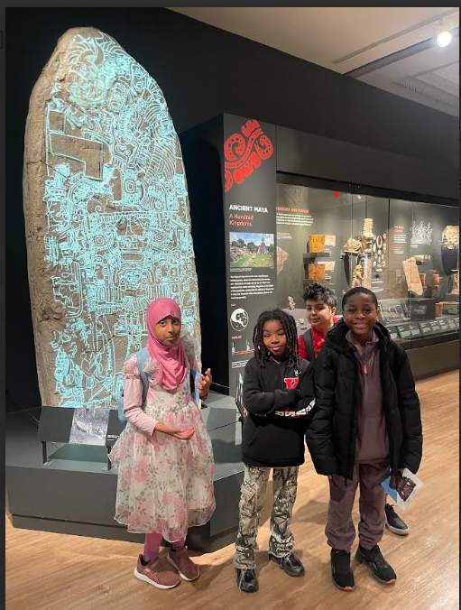 Group of students pose in front of a glowing stone monument in a museum’s Ancient Maya exhibit.