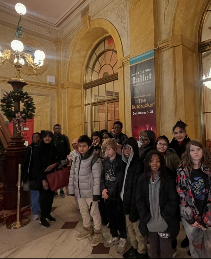 Students stand in a theater lobby next to a banner for The Nutcracker by the Philadelphia Ballet.