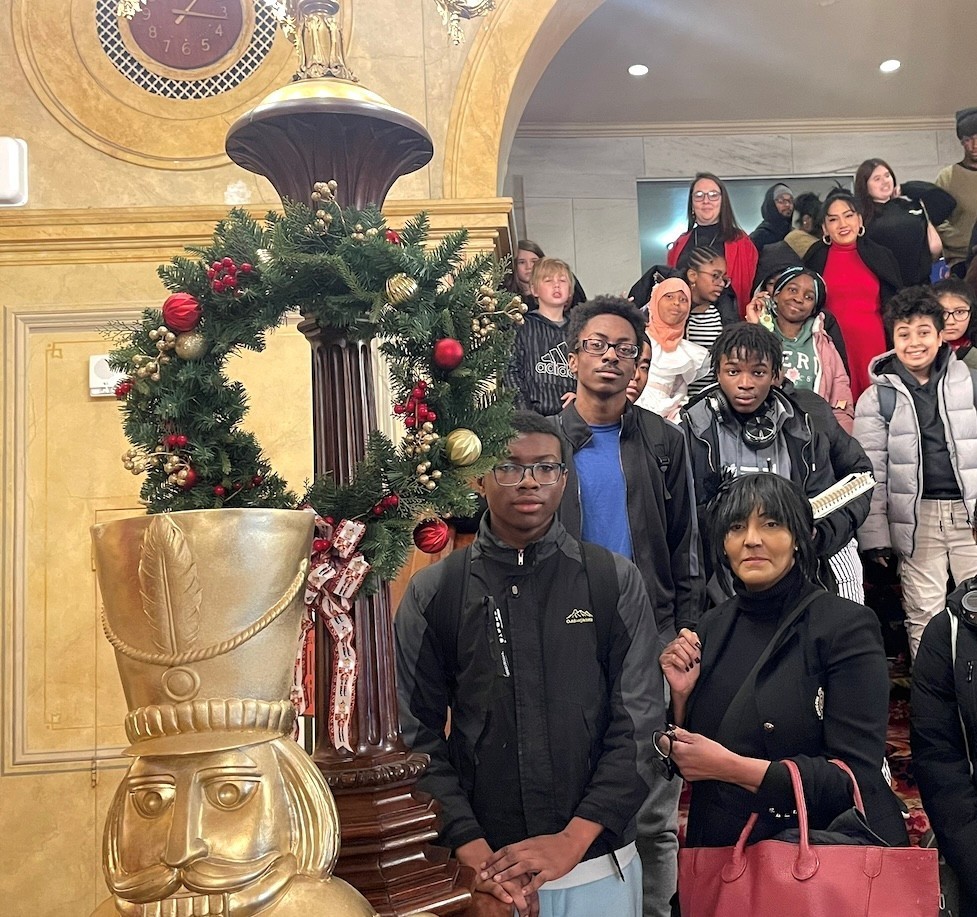 Students and chaperones pose by a holiday wreath and Nutcracker statue in an ornate theater lobby.