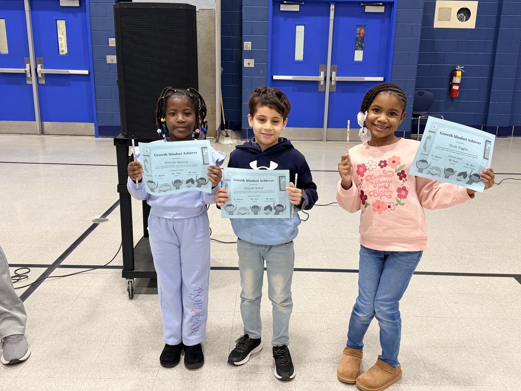 Three students hold “Growth Mindset Achiever” certificates and pencils in the gym.