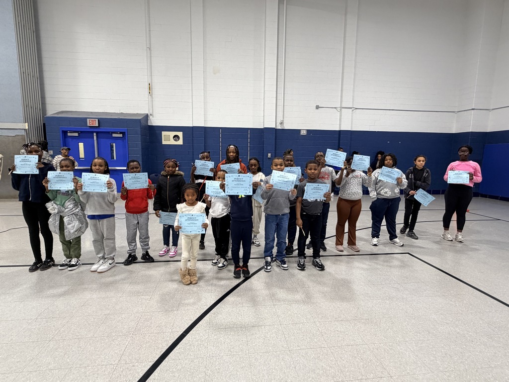 Students line up across the gym floor holding achievement certificates and smiling.
