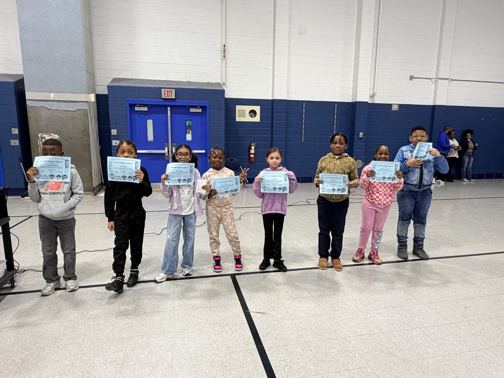 Eight children standing in a gymnasium holding certificates, smiling and posing for a group photo.