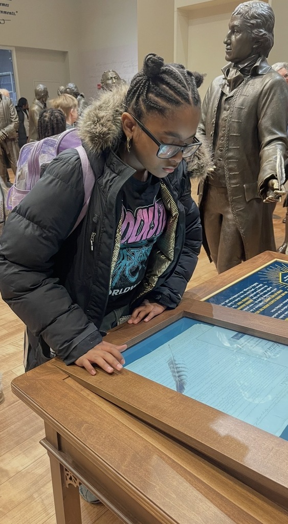 Young person in a black jacket with braided hair closely examining a historical document display in a museum setting.