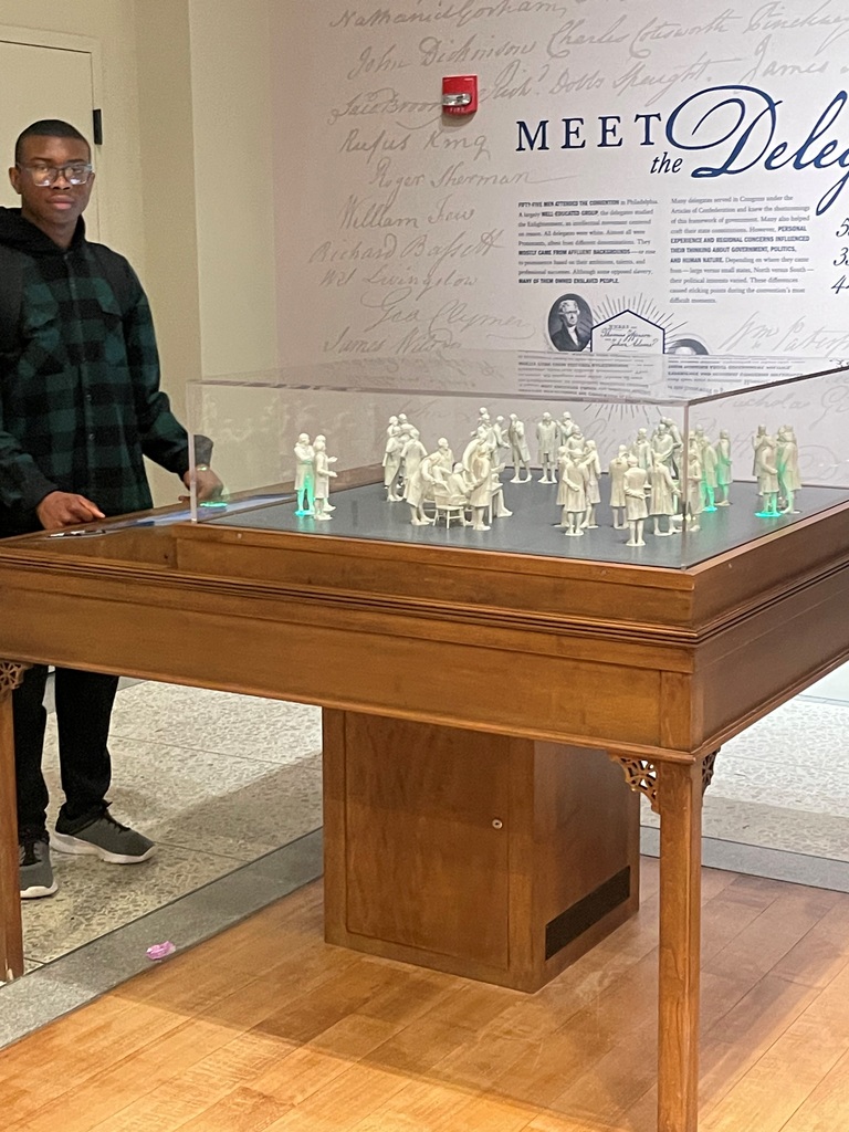 Display case with miniature white figurines representing historical delegates at a museum exhibit titled 'Meet the Delegates'.