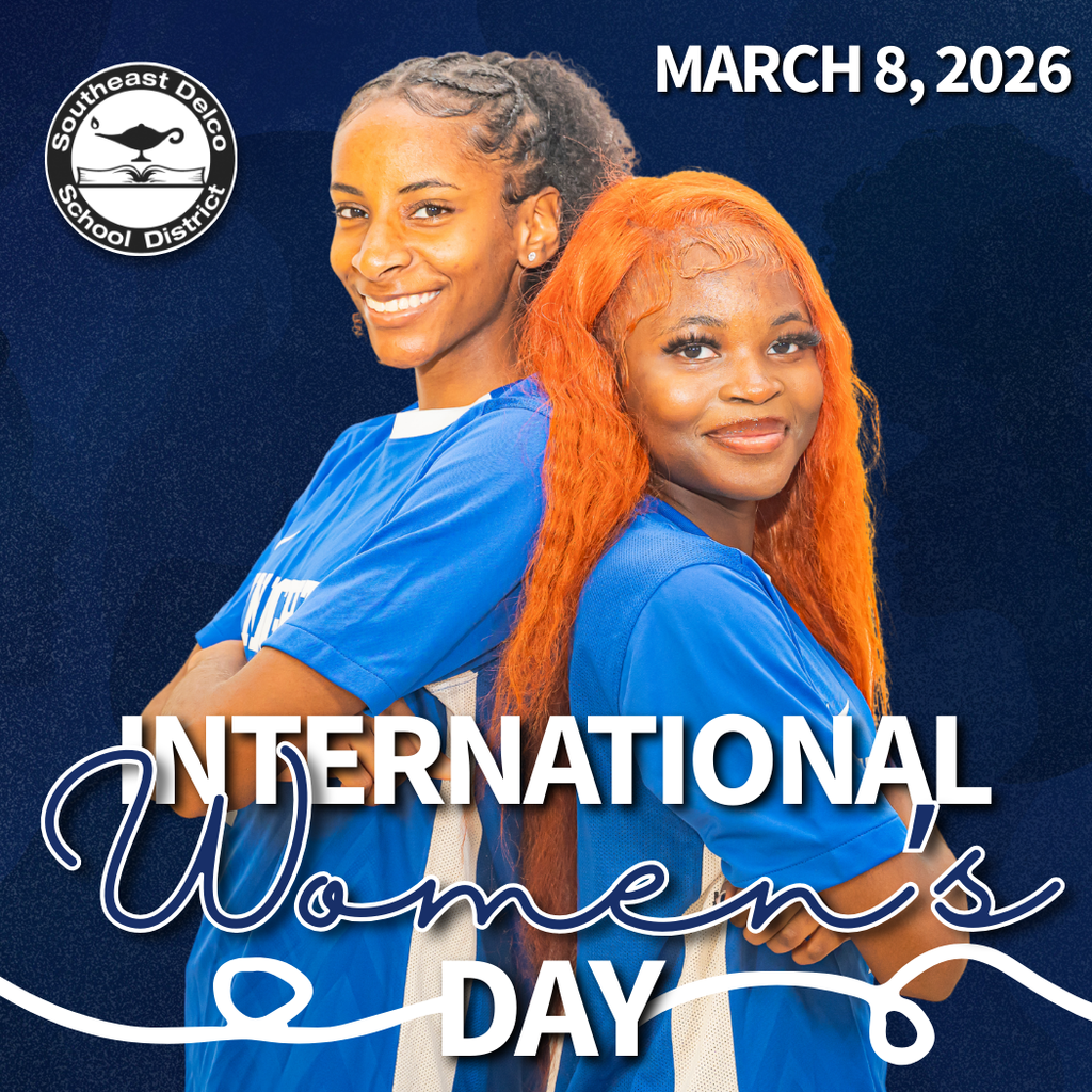 Two women in blue shirts stand back to back with arms crossed against a dark blue background celebrating International Women's Day on March 8, 2026.