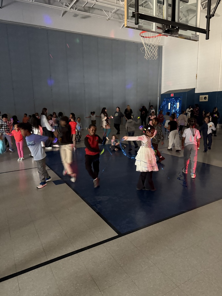 Children dancing and socializing in a school gymnasium under a basketball hoop.