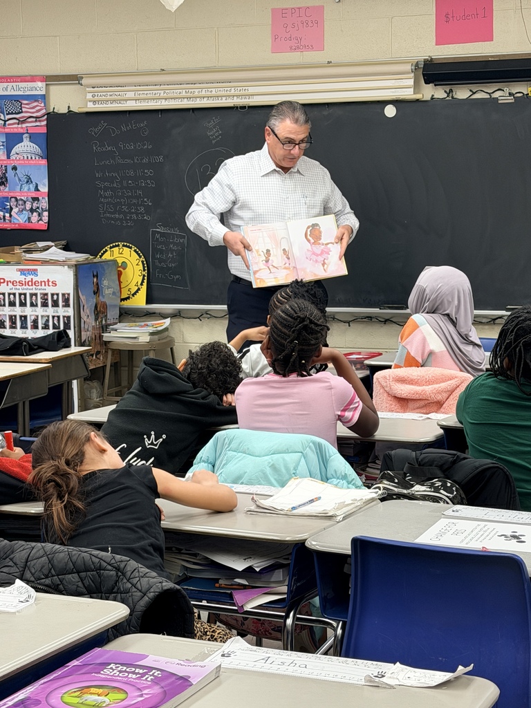 Teacher reading a picture book aloud to attentive elementary students seated at desks in a classroom.