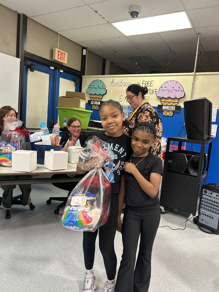 Two students stand together smiling, holding a clear bag filled with snacks and prizes during a school event.